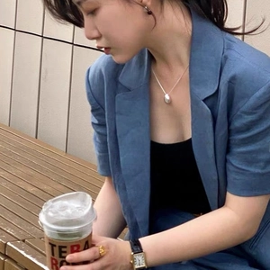 Lifestyle shot of a minimalist silver teardrop pendant necklace worn with a blue blazer