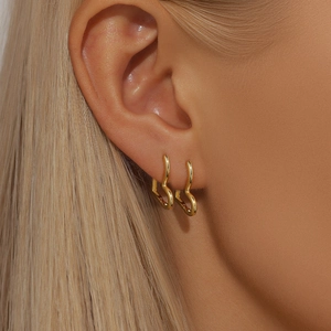 Detail of model wearing gold heart-shaped punk stud earrings with rivet texture