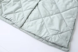 Detail of light green quilted vest featuring diamond patterns and round snap buttons