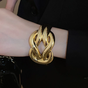 Close-up of a wide polished gold crisscross cuff bracelet with bold minimalist design