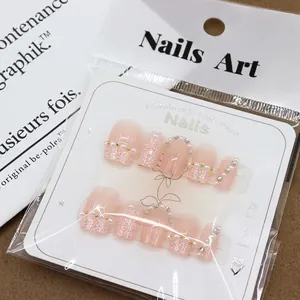 Pink and white tweed press-on nails with pearls and rhinestones on sizing card