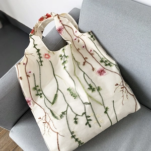 Close-up of intricate floral embroidery and plant vine details on a cream canvas tote bag