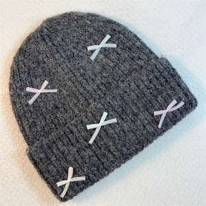 Detail of dark grey knit beanie with colorful ribbon bows on a textured background