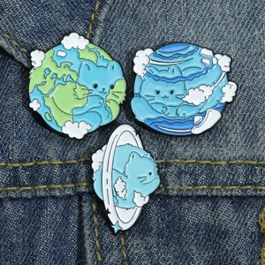 Set of three cute enamel cat planet brooches on dark blue denim fabric background