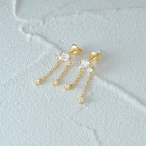 Detail of gold tassel earrings featuring sparkling round stones on a textured background