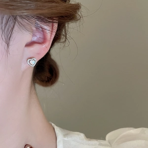 Close-up of heart-shaped silver stud earring with iridescent opal and pavé crystals