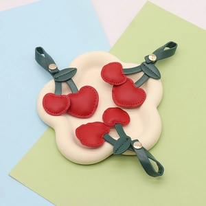 Three red leather cherry keychains with green leaves on a cloud-shaped plate