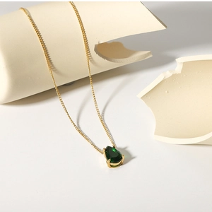 Artistic detail of 18k gold plated water drop green zircon pendant on beige ceramics