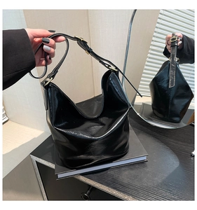 Detail of glossy black patent leather bucket bag with adjustable strap and gold hardware