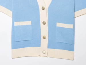 Close-up of sky blue knit cardigan with gold embossed buttons and white contrast pockets
