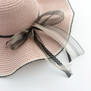 Pink straw sun hat with wavy brim featuring black and white polka dot ribbon and bow