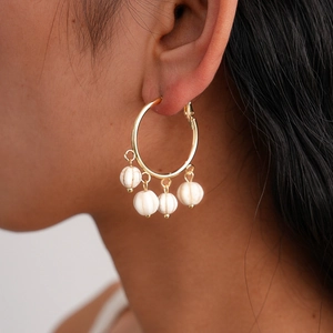 Detail view of gold hoop earrings with white marble bead tassels on a model's ear