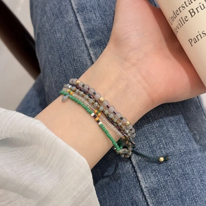 Close-up of bohemian layered seed bead bracelet featuring mixed green and gold tones