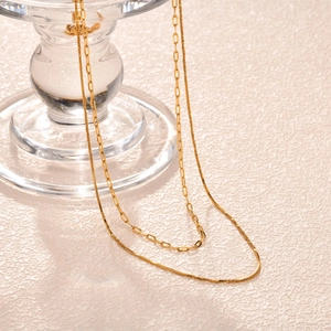 Detailed view of layered gold snake chain and paperclip link necklace on glass stand