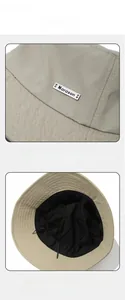Detail of a beige bucket hat showing its metal brand tag and premium breathable lining