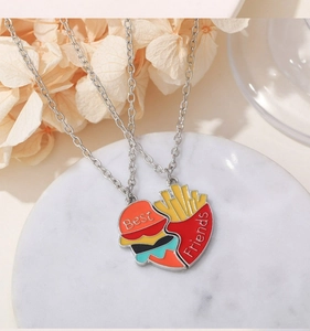 Detail of Best Friends hamburger and fries heart-shaped enamel necklaces on marble base
