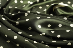 Close-up of dark green polka dot silk satin scarf fabric showing soft drape and glossy texture