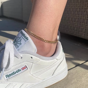 Gold-plated Cuban link anklet and beaded chain set worn on woman's ankle in sunlight