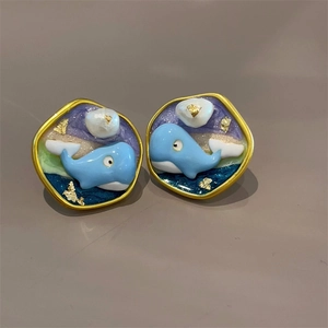 Detail of whale-shaped enamel earrings with blue-purple gradients and gold foil flakes