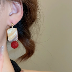 Close-up of model wearing square shell pendant earrings with elegant red beads