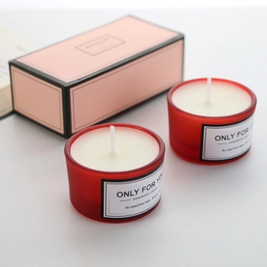 Dettaglio di candele profumate in vetro satinato rosso in una confezione regalo rosa chic