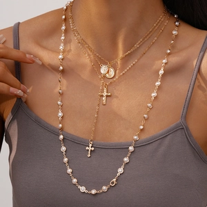 Layered gold necklace featuring cross pendant, vintage medals and white pearls on a model