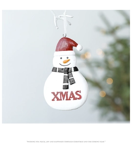 Close-up of resin snowman ornament with red XMAS text and festive ribbon on a lit Xmas tree