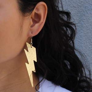Macro side view of a model wearing large hollow lightning bolt golden metal earrings
