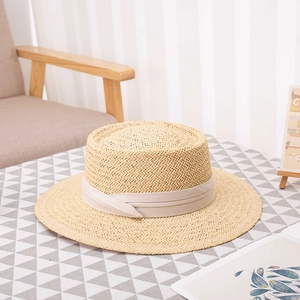 Handwoven straw boater hat with wide brim and beige ribbon band on a checkered table