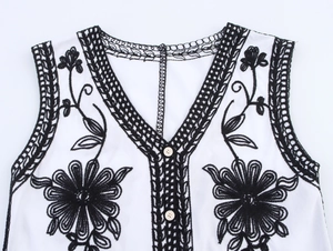 Detail of V-neckline featuring black floral embroidery and woven lace on white vest
