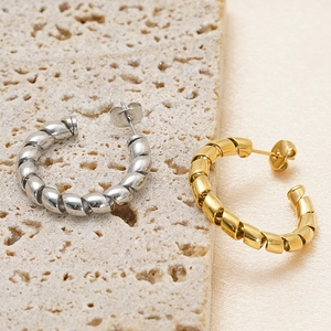 Twisted rope design hoop earrings in gold and silver finish on a neutral stone slab