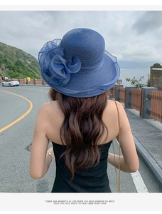 Close-up of elegant blue sun hat with large floral decor on a scenic coastal road