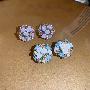 Close-up of cluster flower earrings in light purple and blue-white with golden crystals