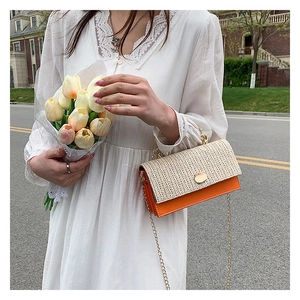 Detail of woven straw flap and orange faux leather crossbody bag with gold chain