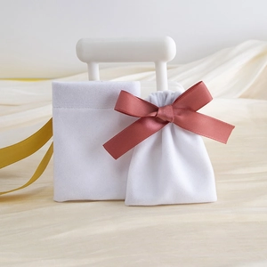 White velvet jewelry pouch set with elegant pink ribbon bow on beige silk backdrop