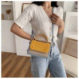 Detail of color-block patchwork shoulder bag with adjustable strap worn by model