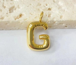 Close-up of a 3D gold puffy bubble letter G pendant with a polished metallic finish