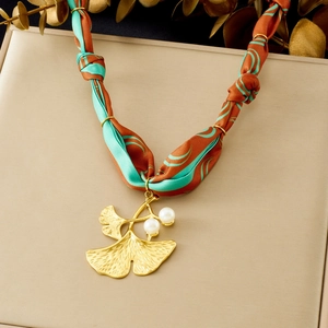 Detail of gold ginkgo leaf pendant with pearls on orange and green ribbon silk necklace