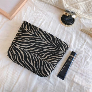 Detail shot of a soft knit zebra stripe makeup bag and fashion clutch on white background
