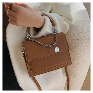 Brown leather crossbody bag with chain detail and circular charm held by model
