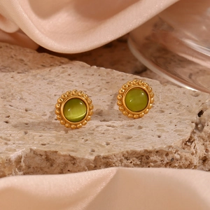 Macro shot of gold sun earrings featuring green cat eye stones on textured stone