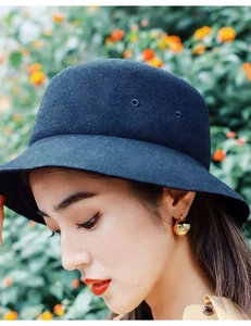 Model wearing a deep blue wool felt dome cloche hat against a blurred floral background