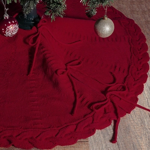 Red knitted Christmas tree skirt with cable knit pattern and tie closure on wood floor