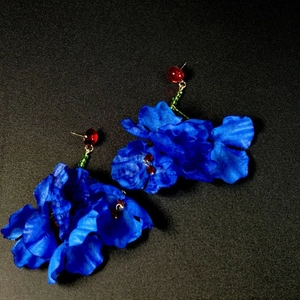 Détail de boucles d'oreilles fleuries en tissu bleu avec perles rouges et pompons