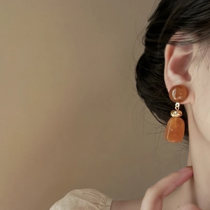 Close-up of amber resin geometric earrings with gold twisted metal knot on model