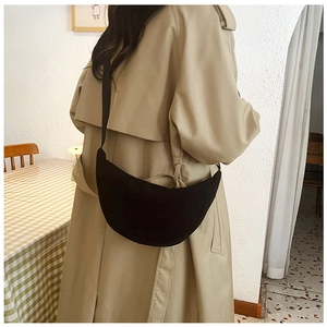 Close-up of black corduroy crescent bag worn over a beige trench coat in a home setting