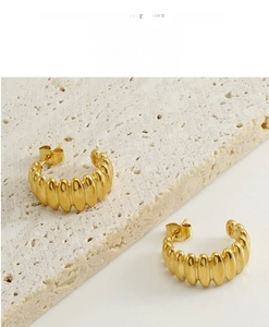 Détail de boucles d'oreilles créoles dorées 18k avec texture ondulée sur pierre blanche