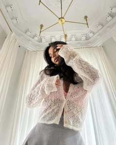 Detail of off-white hollow knit cardigan featuring lace texture and amber buttons