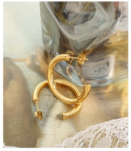 Detail of chunky gold-plated C-shaped hoop earrings with polished finish on lace backdrop