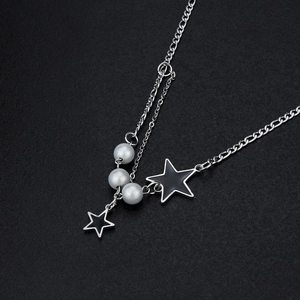 Gros plan d'un collier chaîne argentée avec pendentifs étoiles noires et perles blanches